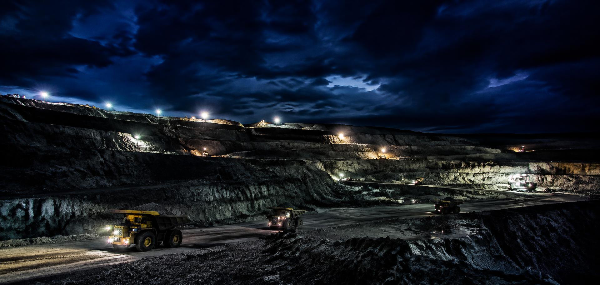 Working open-cut mine at night with floodlights and haul trucks